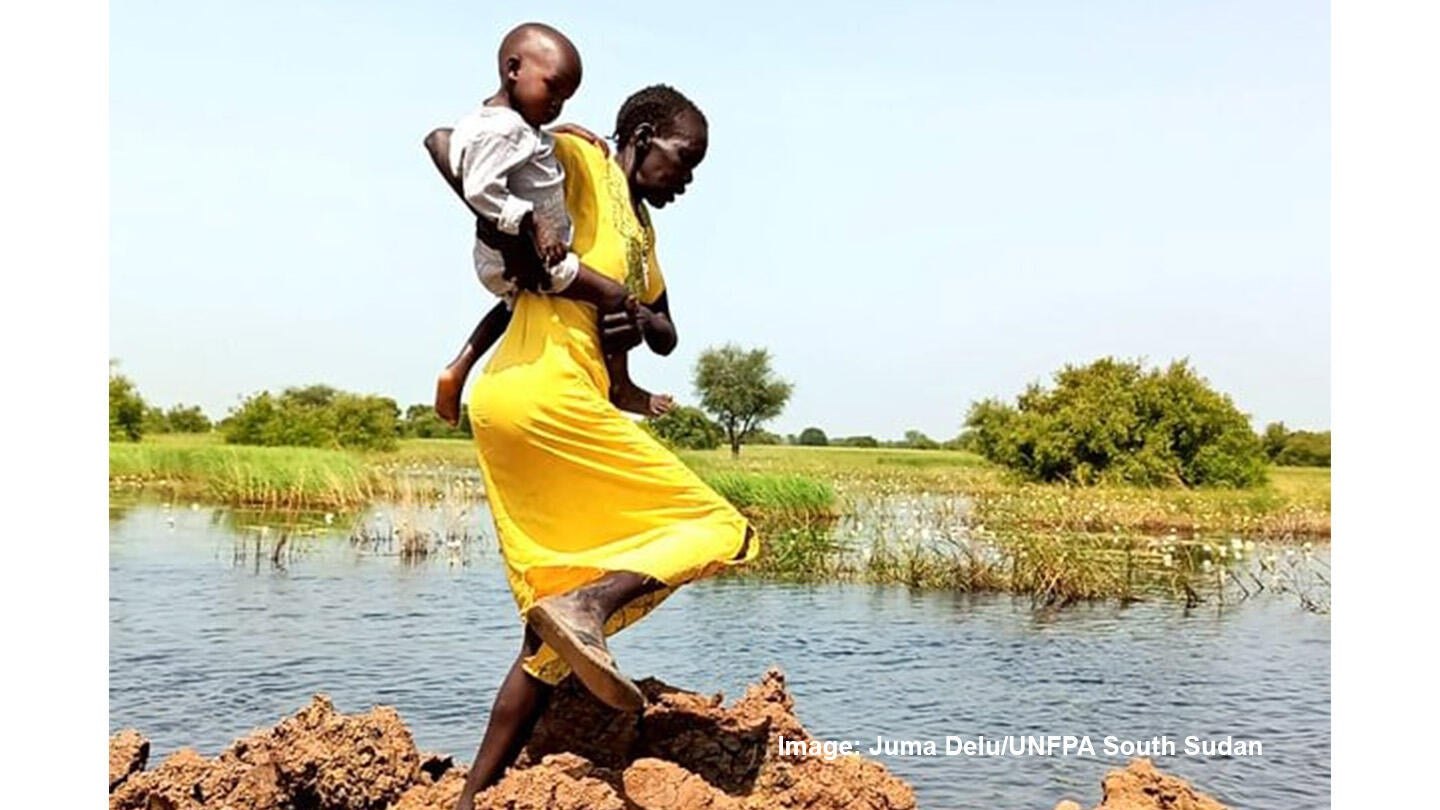 A mother with her baby crossing flooded road in Malualkon